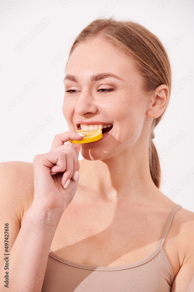 beautiful blonde woman laying on a white wooden background next to slices of lemon, having a slice of lemon on the eyes and smiling beautiful blonde woman laying on a white wooden background next to slices of lemon, having a slice of lemon on the eyes and smiling
