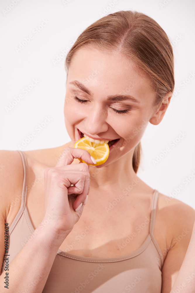 beautiful blonde woman laying on a white wooden background next to slices of lemon, having a slice of lemon on the eyes and smiling beautiful blonde woman laying on a white wooden background next to slices of lemon, having a slice of lemon on the eyes and smiling