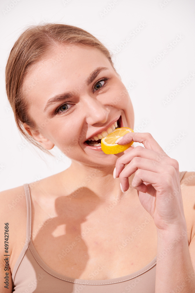 beautiful blonde woman laying on a white wooden background next to slices of lemon, having a slice of lemon on the eyes and smiling beautiful blonde woman laying on a white wooden background next to slices of lemon, having a slice of lemon on the eyes and smiling