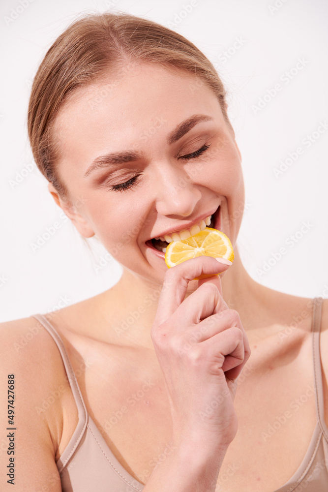 beautiful blonde woman laying on a white wooden background next to slices of lemon, having a slice of lemon on the eyes and smiling beautiful blonde woman laying on a white wooden background next to slices of lemon, having a slice of lemon on the eyes and smiling