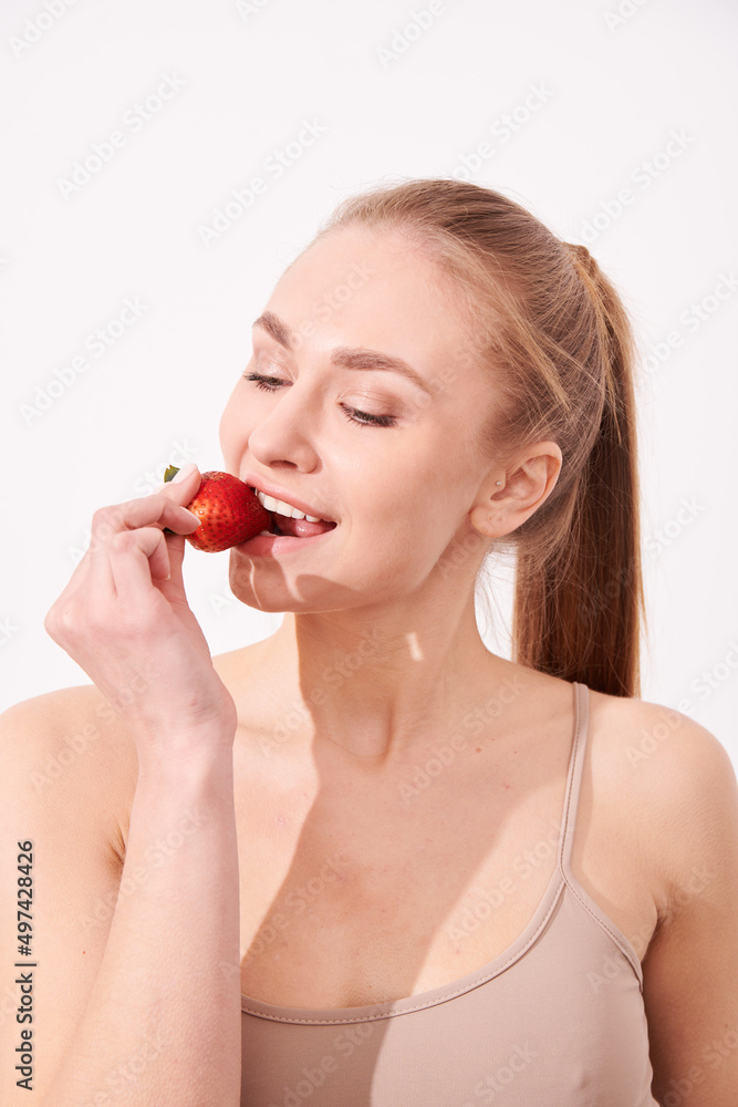 A creative portrait of a beautiful girl holding with one hand a juicy strawberry near her lips with temptation. A creative portrait of a beautiful girl holding with one hand a juicy strawberry near her lips with temptation.