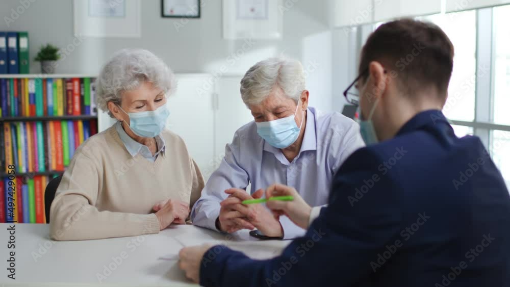 Senior couple in safety mask signing on document in real estate agent office Senior couple in safety mask signing on document in real estate agent office