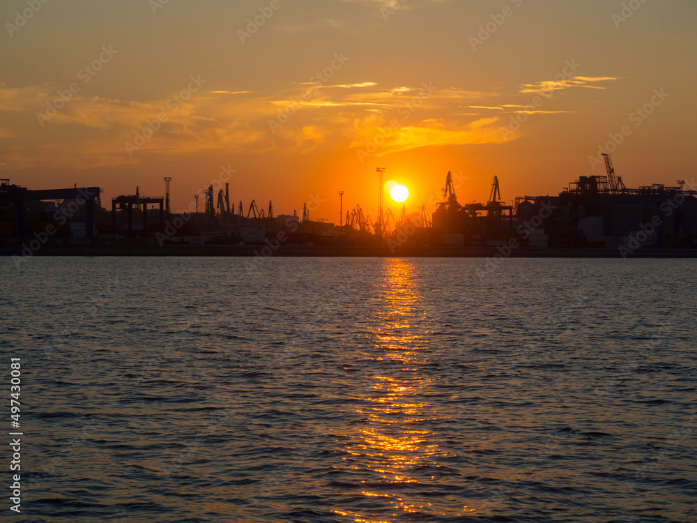 Beautiful sunset above port on sunset time with silhouettes of cargo cranes. Industrial black sea port Odesa, Ukraine with a lot of cranes, cabins, boxes and tanks by the water on colorful sunset