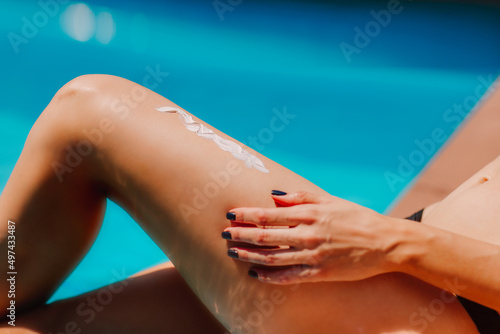 Woman's legs with sun cream on it against blue swimming pool. Skin care concept. © Liudmila