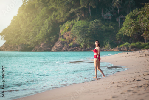 Young beauty asian woman in dress happy travel smile walk on beach sea near blue water wave for trip vacation. Summer day tan skin girl happy in red bikini smiling at sunbath on koh chang, Thailand.