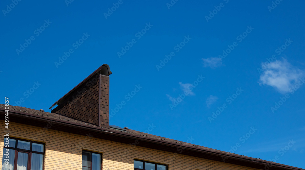 A roof with a chimney on the background of a blue summer sky. Place for your text