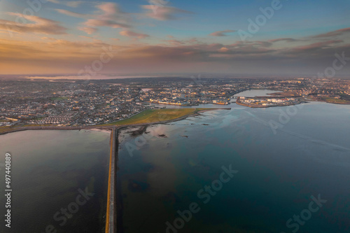 Causeway to Mutton island and Galway bay, town center in the background, Cloudy sky. Ireland. Blue ocean water at sunset. Irish landscape. Aerial view