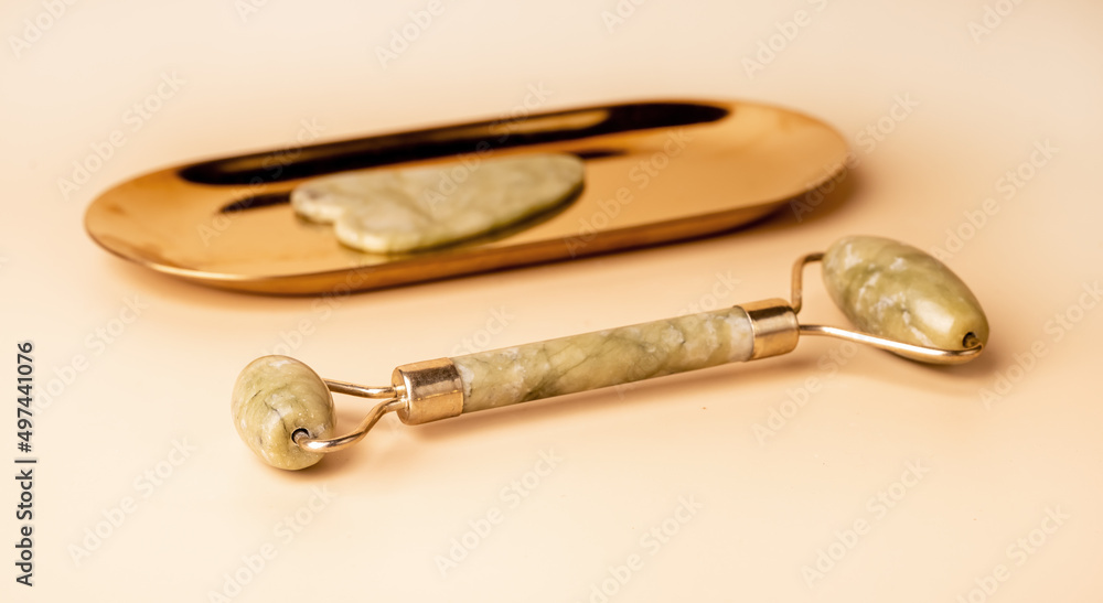 Gua Sha massage tools. Scraper and roller on golden stand and on beige background. Instruments for acupuncture therapy, trigger point treatment. High quality photo Gua Sha massage tools. Scraper and roller on golden stand and on beige background. Instruments for acupuncture therapy, trigger point treatment. High quality photo