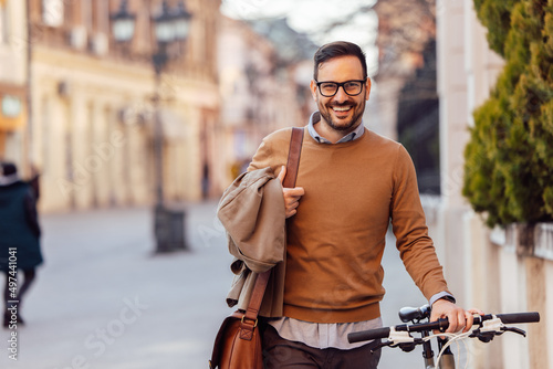 Portrait of smiling stylish caucasian man, carrying his jacket, holding his bike © bnenin