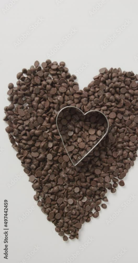 Vertical video of chocolate chips forming heart with heart shaped cookie cutter on white background Vertical video of chocolate chips forming heart with heart shaped cookie cutter on white background