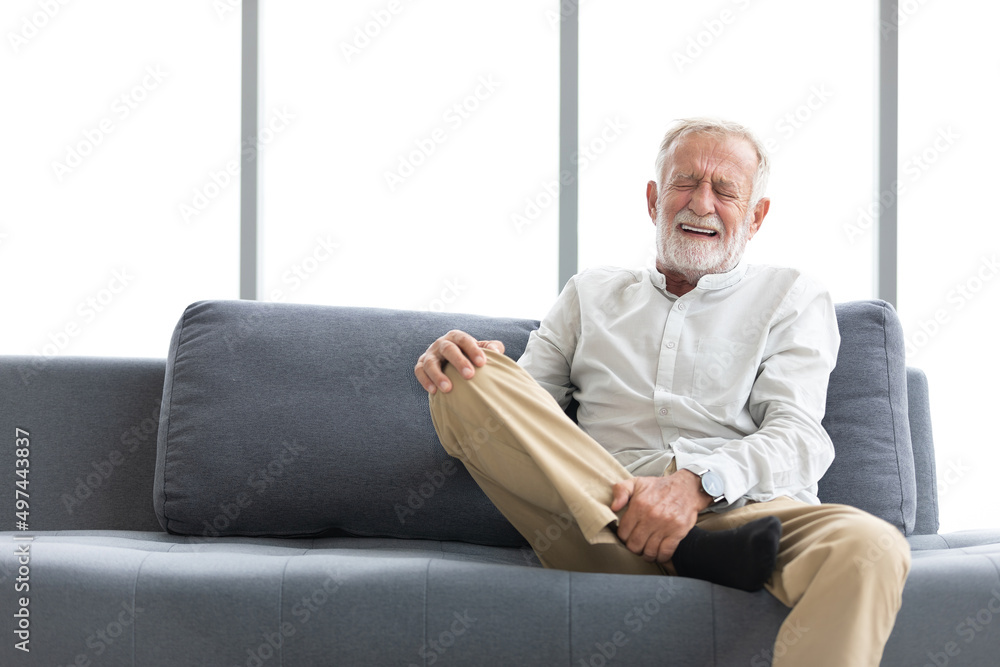 senior man suffering from knee ache on sofa