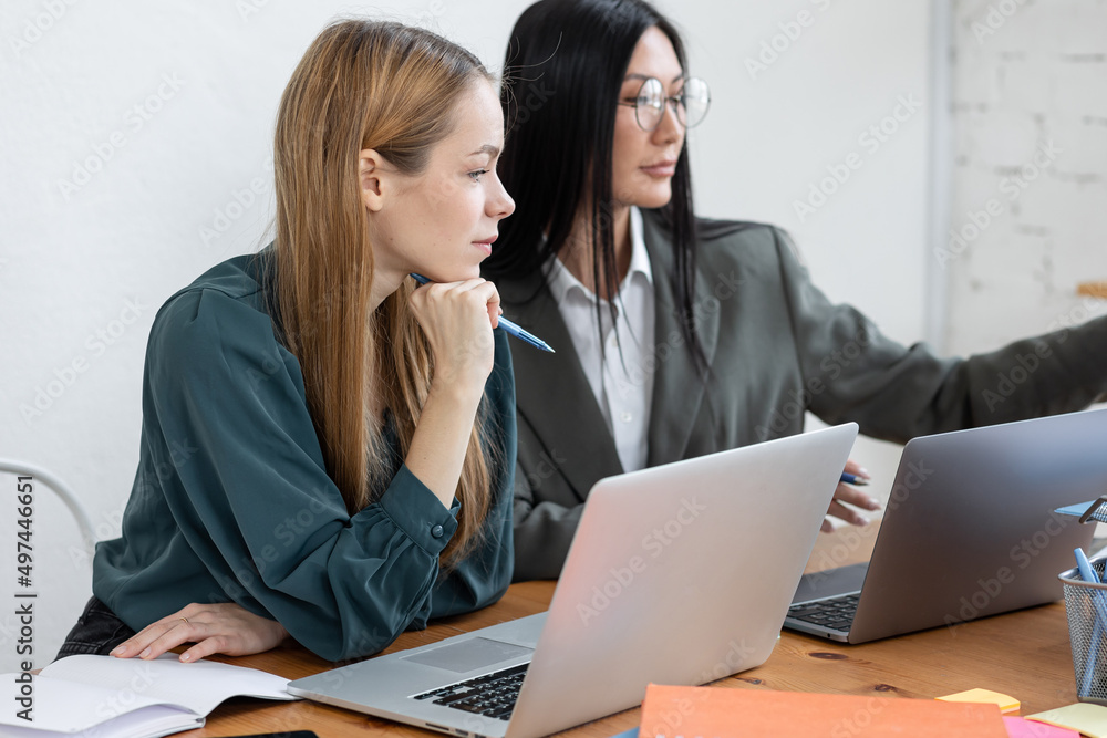 Two young women in office. Talking, discussion, team work, collaboration. Diversity, asian female. Concept of job in corporation, young professionals. Finance, marketing Two young women in office. Talking, discussion, team work, collaboration. Diversity, asian female. Concept of job in corporation, young professionals. Finance, marketing