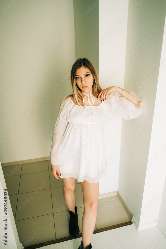 Portrait of attractive caucasian young woman in a white dress standing in a empty room with white walls. Portrait of attractive caucasian young woman in a white dress standing in a empty room with white walls.