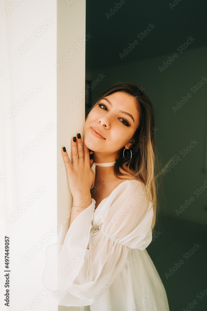 Portrait of attractive caucasian young woman in a white dress standing in a empty room with white walls. Portrait of attractive caucasian young woman in a white dress standing in a empty room with white walls.