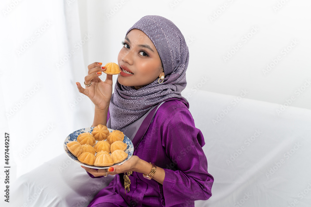 Muslim girl celebrates end of Ramadan, in purple kebaya dress with hijab, and holding bahulu food, white background, portrait waist up Muslim girl celebrates end of Ramadan, in purple kebaya dress with hijab, and holding bahulu food, white background, portrait waist up
