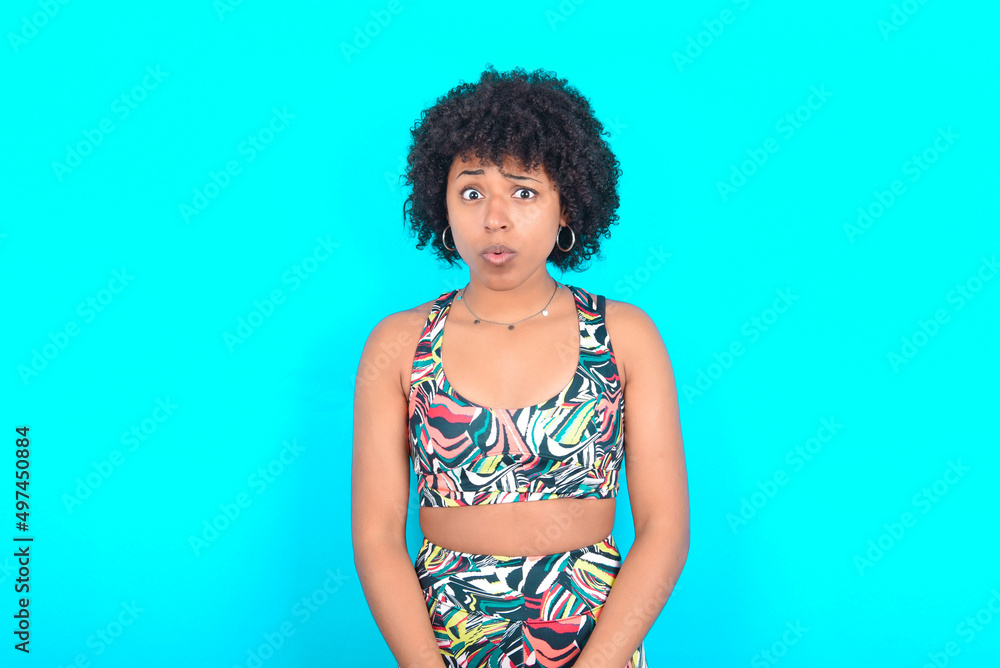 young woman with afro hairstyle in sportswear against blue background expressing disgust, unwillingness, disregard having tensive look frowning face, looking indignant with something. young woman with afro hairstyle in sportswear against blue background expressing disgust, unwillingness, disregard having tensive look frowning face, looking indignant with something.