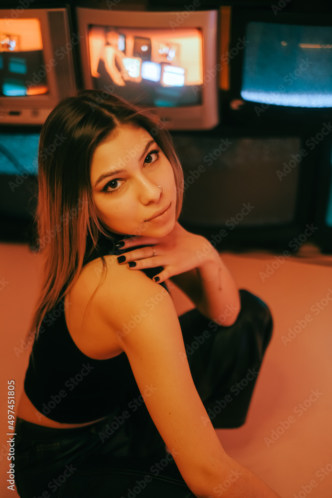 Portrait of young attractive caucasian woman in stylish outfit posing near stand with retro tvs.