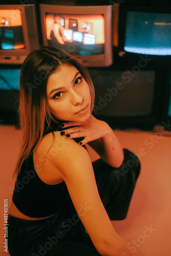 Portrait of young attractive caucasian woman in stylish outfit posing near stand with retro tvs.