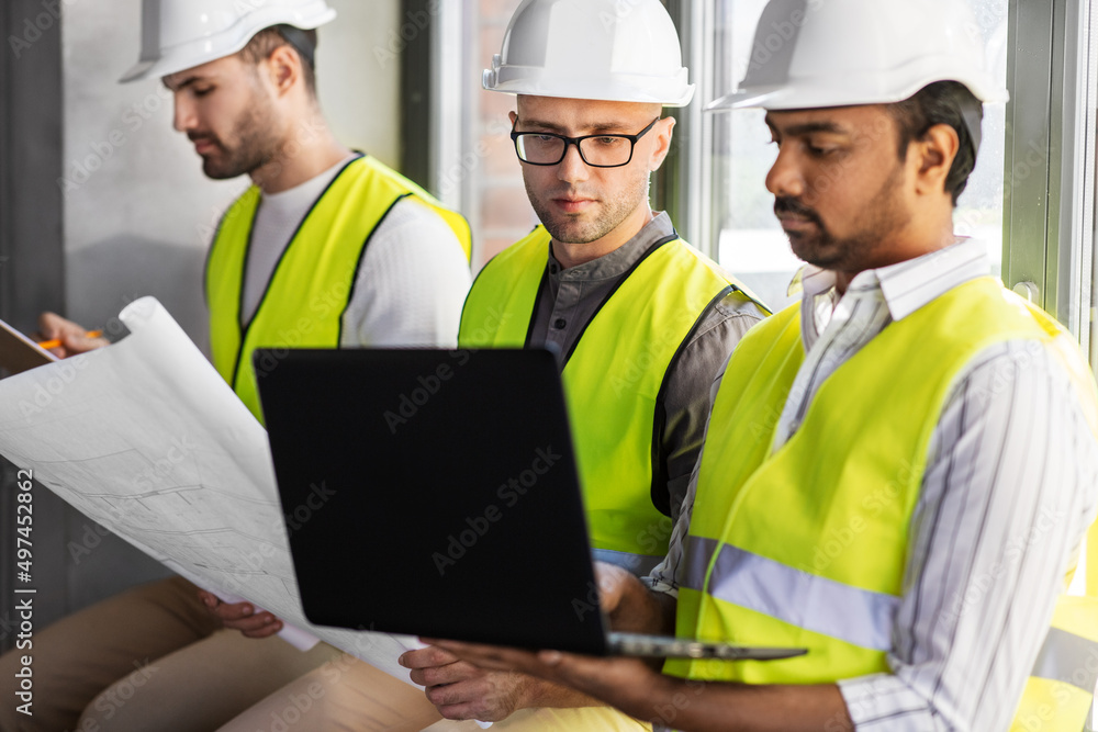architecture, construction business and people concept - group of male architects in helmets with laptop, blueprint and clipboard working at office architecture, construction business and people concept - group of male architects in helmets with laptop, blueprint and clipboard working at office