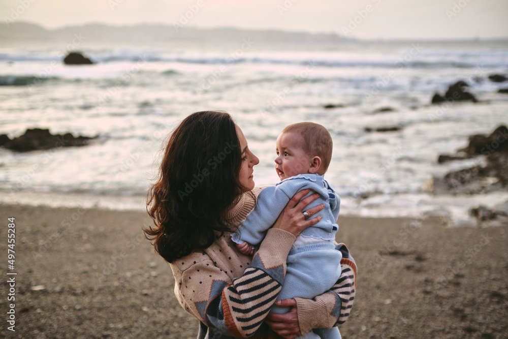 Single young mother holding and looking at her baby on the beach Single young mother holding and looking at her baby on the beach