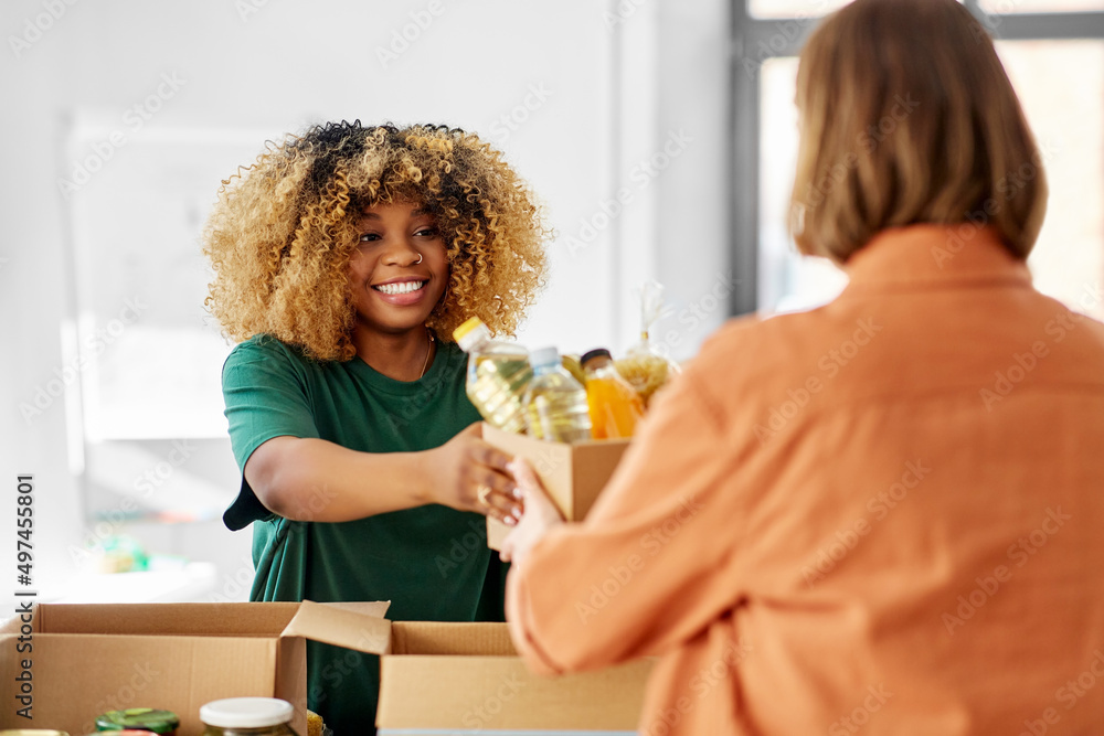 © Syda Productions - charity, donation and volunteering concept - happy smiling female volunteer and woman taking box of food at distribution or refugee assistance center
