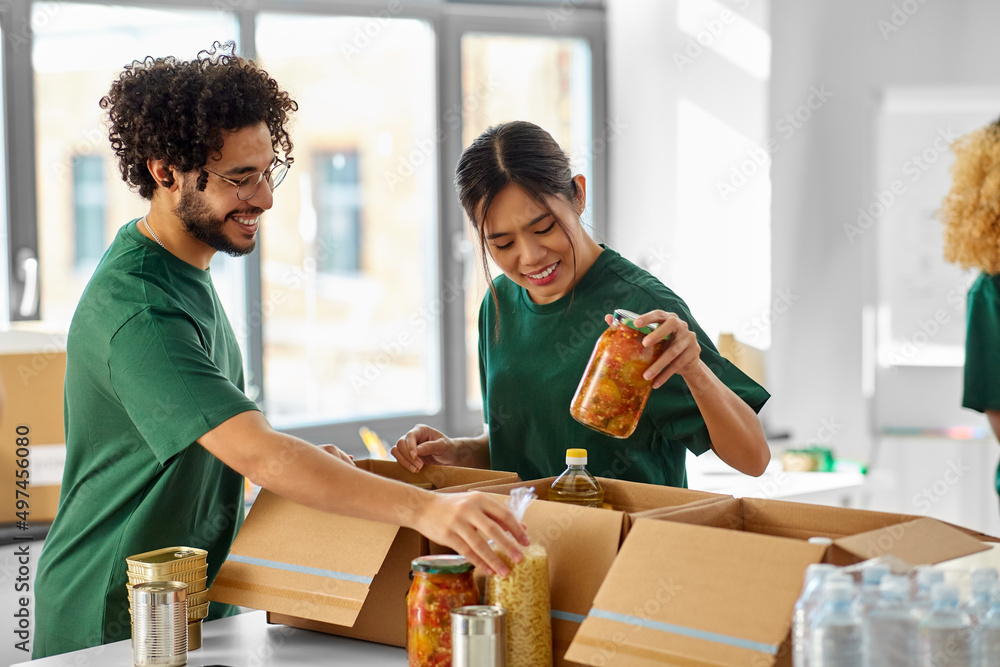 charity, donation and volunteering concept - happy smiling volunteers packing food in boxes at distribution or refugee assistance center charity, donation and volunteering concept - happy smiling volunteers packing food in boxes at distribution or refugee assistance center
