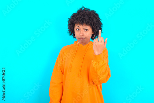 Quadro su tela young woman with afro hairstyle wearing orange hoodie against blue background shows middle finger bad sign asks not to bother