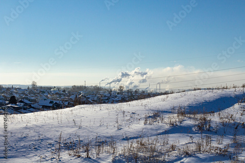 Winter landscape, city view with an industrial plant and large smoking chimneys on a bright sunny day, environmental protection concept