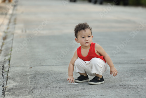 A boy in a red shirt squatting on the street.