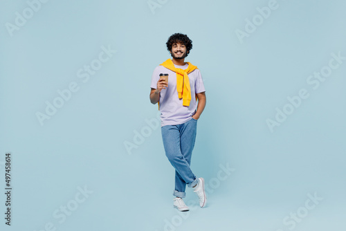 Full size cheerful young bearded Indian man 20s years old wears white t-shirt hold takeaway delivery craft paper brown cup coffee to go isolated on plain pastel light blue background studio portrait.