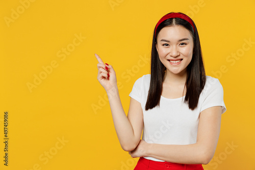 Amazing magnificent young girl woman of Asian ethnicity 20s years old wear white t-shirt pointing finger aside on workspace area copy space mock up isolated on plain yellow background studio portrait