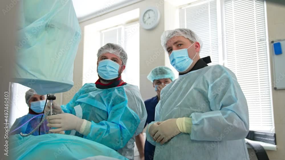 Two surgeons in masks operate the patient and discuss the process. Doctor apply the complicated tool over the patient. Two surgeons in masks operate the patient and discuss the process. Doctor apply the complicated tool over the patient.