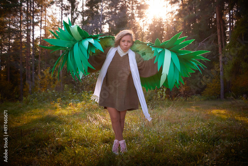 Photos Cute girl in in a grey sweater, white scarf and green wings in nature landscape on sunny autumn