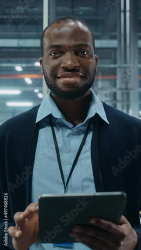 Vertical Screen. Car Factory Office: Portrait of Black Male Chief Engineer Using Tablet Computer in Automated Robot Arm Assembly Line Manufacturing High-Tech Electric Vehicles. Looking at Camera photo