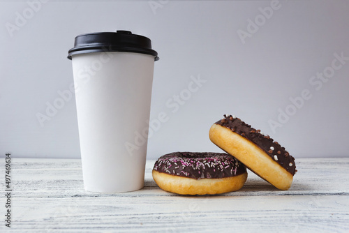 white glass with coffee on a light wooden background with donuts