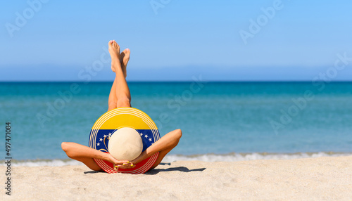 A slender girl on the beach in a straw hat in the colors of the Venezuelan flag. The concept of a perfect vacation in a resort in the Venezuela. Focus on the hat.