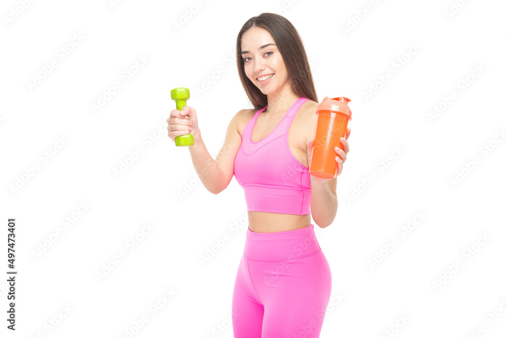 A beautiful, athletic, slim, smiling and cheerful woman in a pink tracksuit holds a dumbbell and a shaker with water. Lifestyle concept with sports and gym. Isolated on white background. A beautiful, athletic, slim, smiling and cheerful woman in a pink tracksuit holds a dumbbell and a shaker with water. Lifestyle concept with sports and gym. Isolated on white background.