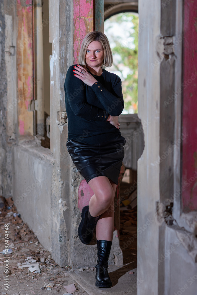 A woman in a leather skirt and a sweater in an abandoned house