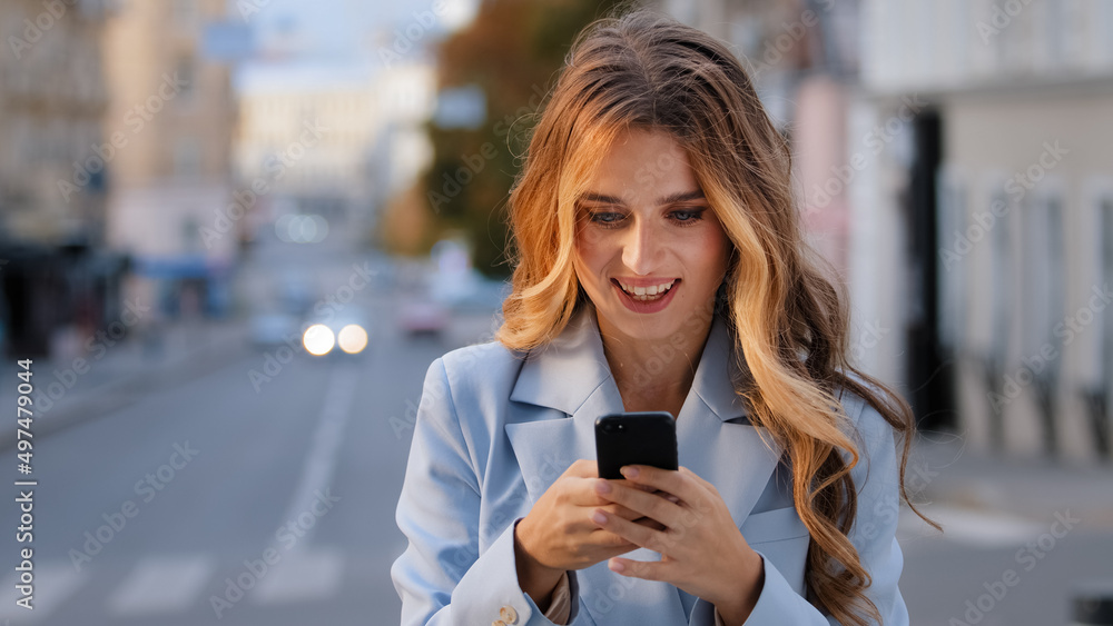 Portrait caucasian girl business woman looking into mobile phone rejoices victory good news chatting in net receives message from boyfriend successful e-commerce buying online standing on city Portrait caucasian girl business woman looking into mobile phone rejoices victory good news chatting in net receives message from boyfriend successful e-commerce buying online standing on city