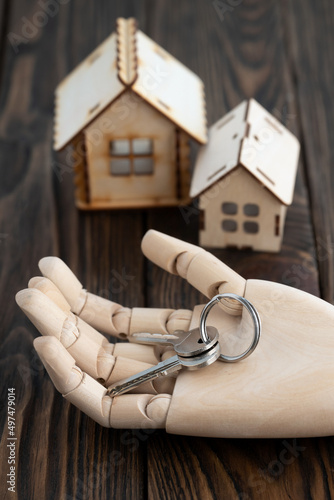 Wooden doll s hand with keys on its palm with toy wooden houses on a background on a table