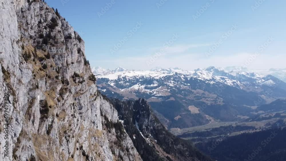 drone flies along steep mountain slopes with the stunning snowy swiss alps in the background in fine sunny weather