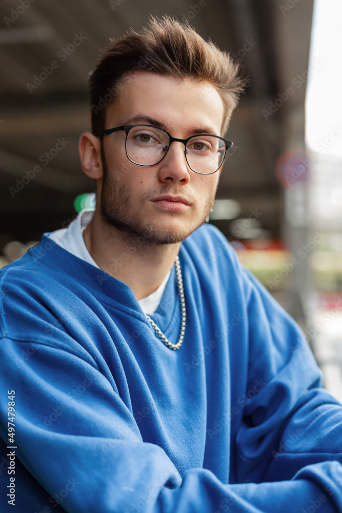 Urban Men's Portrait of a Handsome Hipster Guy with Glasses in a Fashion Blue Sweater in the City Urban Men's Portrait of a Handsome Hipster Guy with Glasses in a Fashion Blue Sweater in the City