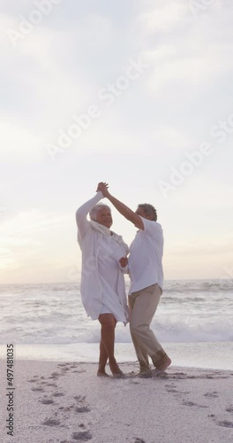 Vertical video of happy senior biracial couple dancing on sunny beach photo