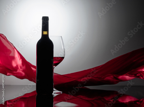 Вottle and glass of red wine on a black reflective background.