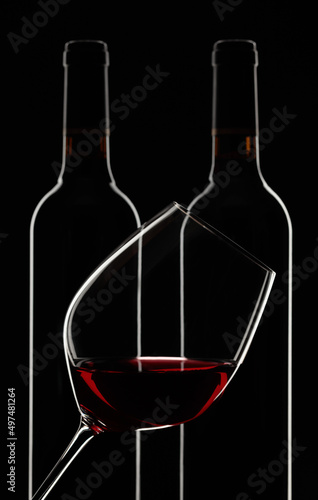 Glass and bottles of red wine on a black background.