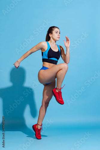 Young beautiful sportive girl training with sports equipment isolated on blue studio background. Sport, action, fitness, youth concept.