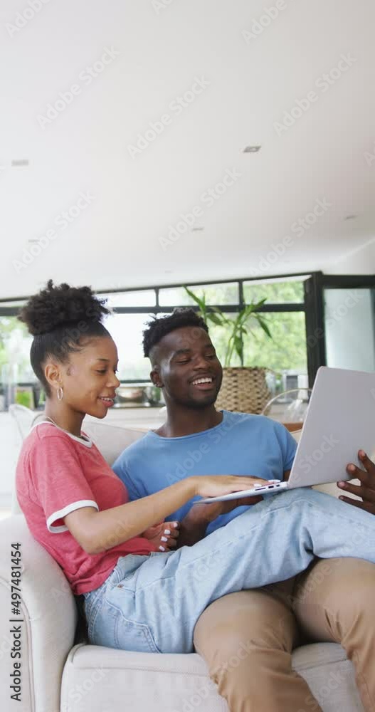 Vertical video of happy african american couple using laptop at home