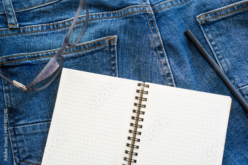A white notebook rests on blue jeans.