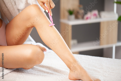 Young woman shaving legs with a razor blade in the bathroom