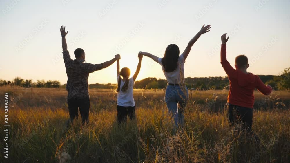 Happy parents with children run through summer grass field holding hands of each other and raising arms. Mommy and daddy with two kids enjoying nature together at sunset. Concept of family happiness Happy parents with children run through summer grass field holding hands of each other and raising arms. Mommy and daddy with two kids enjoying nature together at sunset. Concept of family happiness